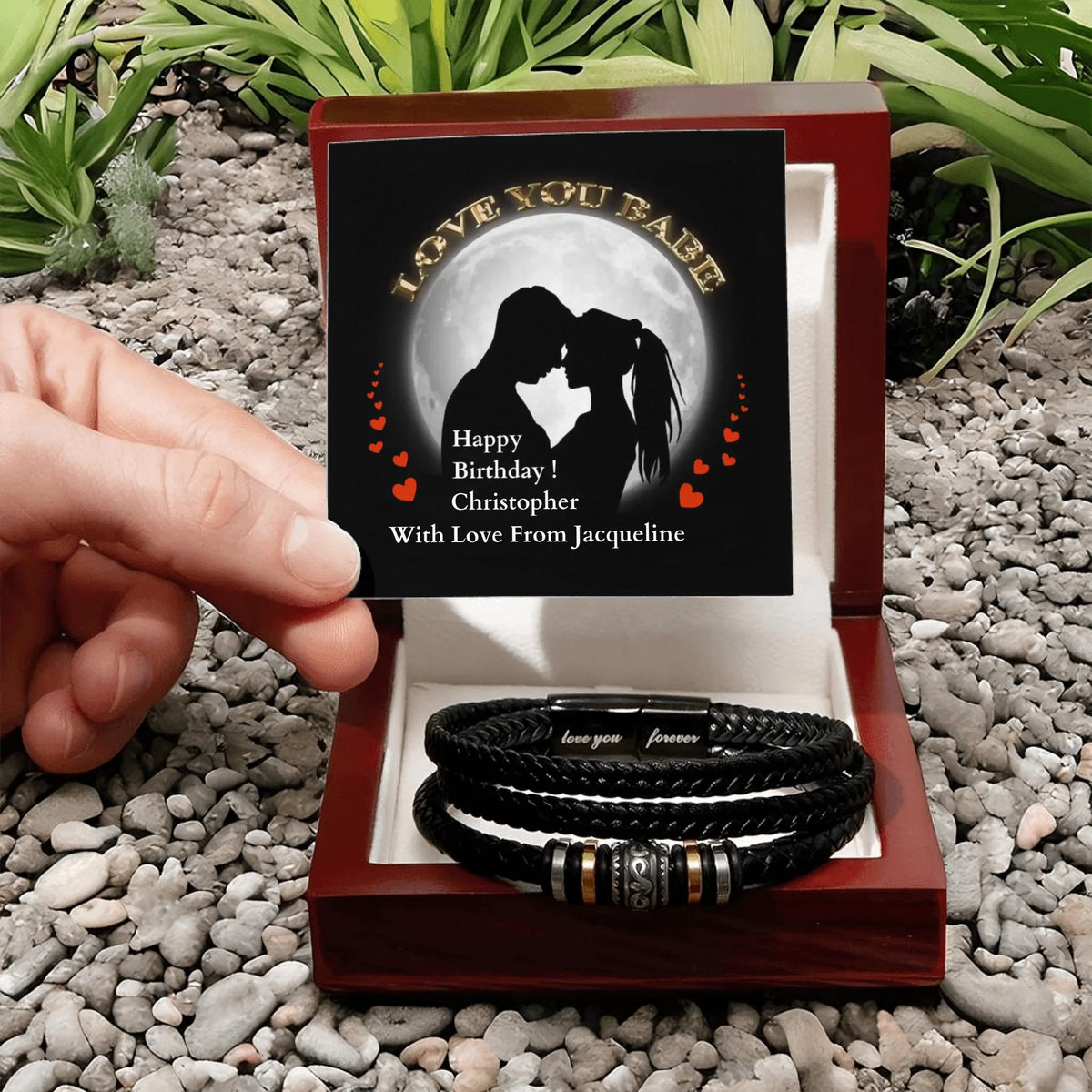 Personalized leather bracelets in a wooden box with an engraved message, set against a natural stone background.