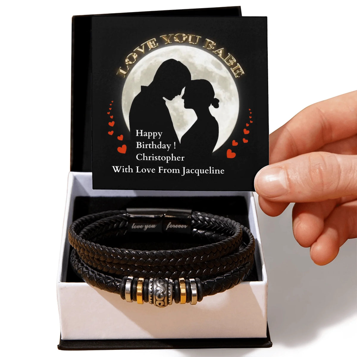 Personalized black leather bracelet with engraved message in a box, held by a hand.