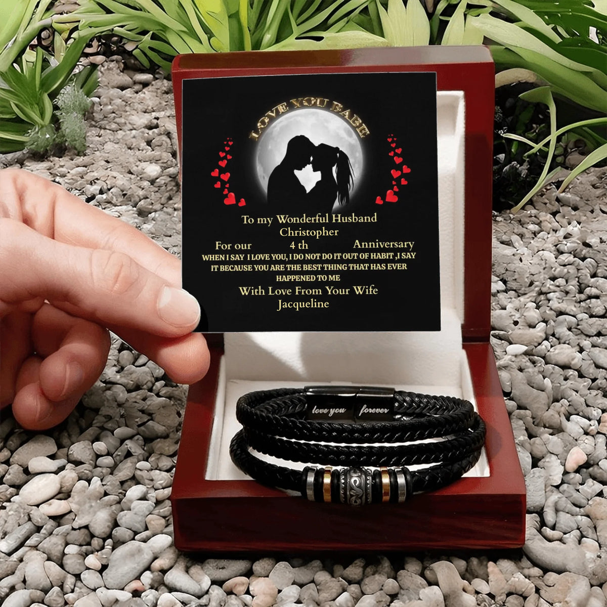 Personalized leather bracelets in a wooden box with a message card on pebbles.
