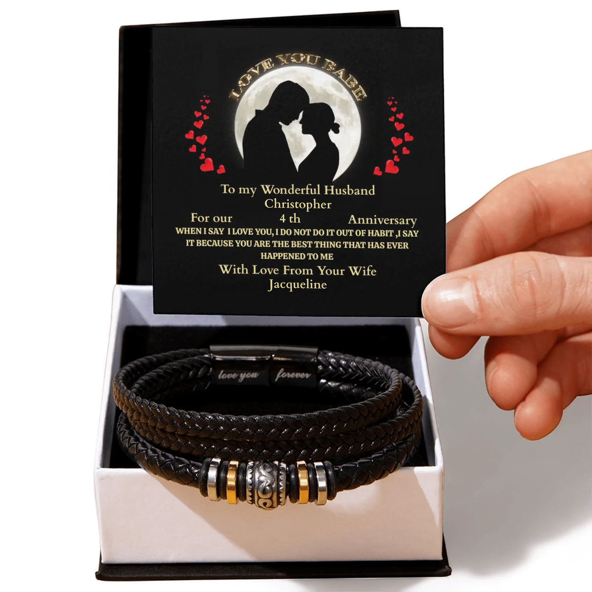 Black leather bracelet with metal charms in a box with a personalized card, held by a hand.