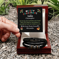 Personalized bracelet set in a wooden box with a Christmas message card on a pebbly surface.