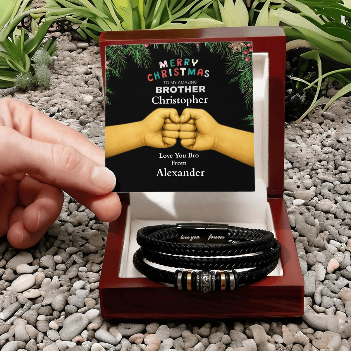 Personalized bracelet set in a decorative box with a Christmas card on a pebbled surface.