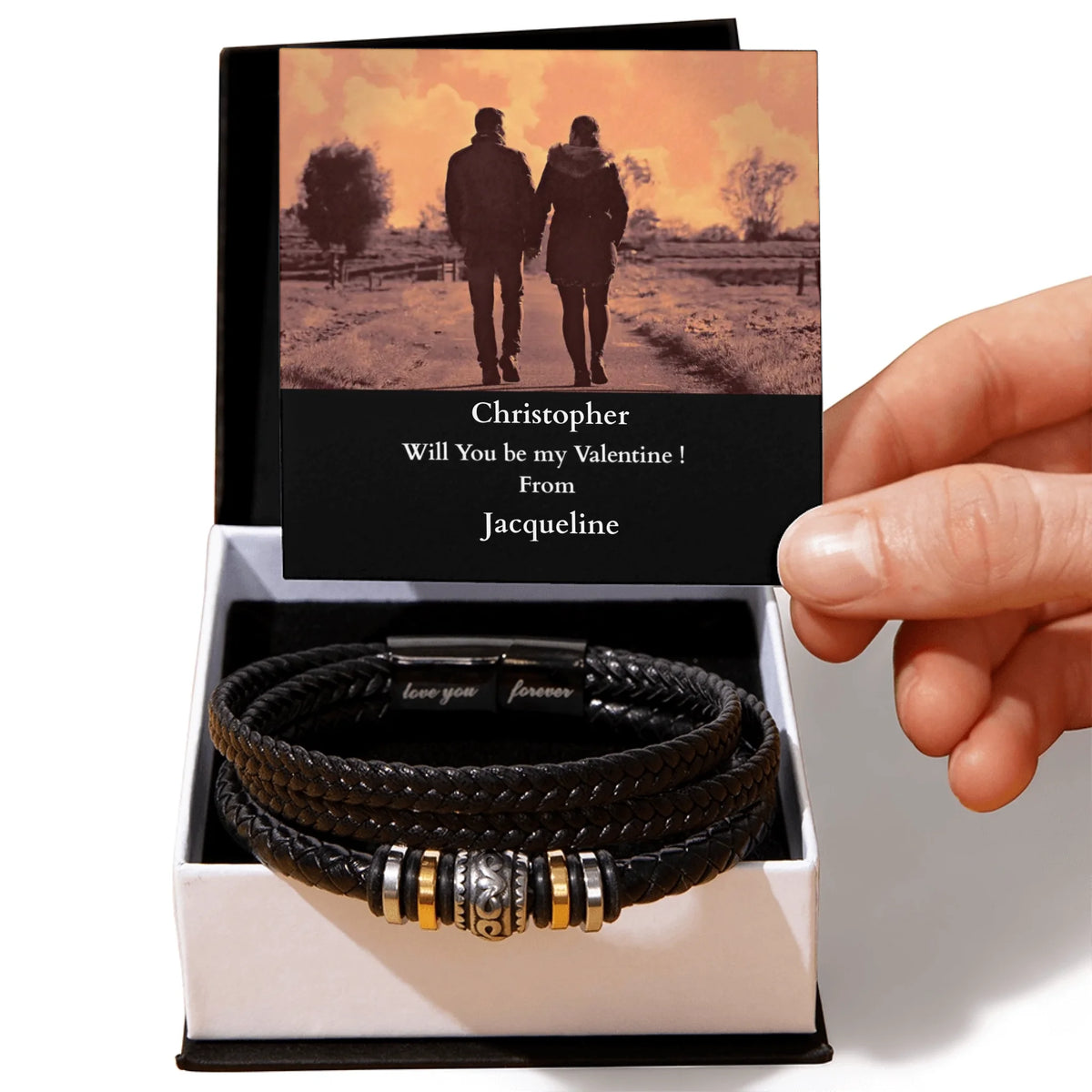 Black leather bracelet with metal accents in a box with a romantic card, held by a hand.