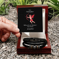 Three black leather bracelets in a wooden box with a Valentine's Day card on pebbles.