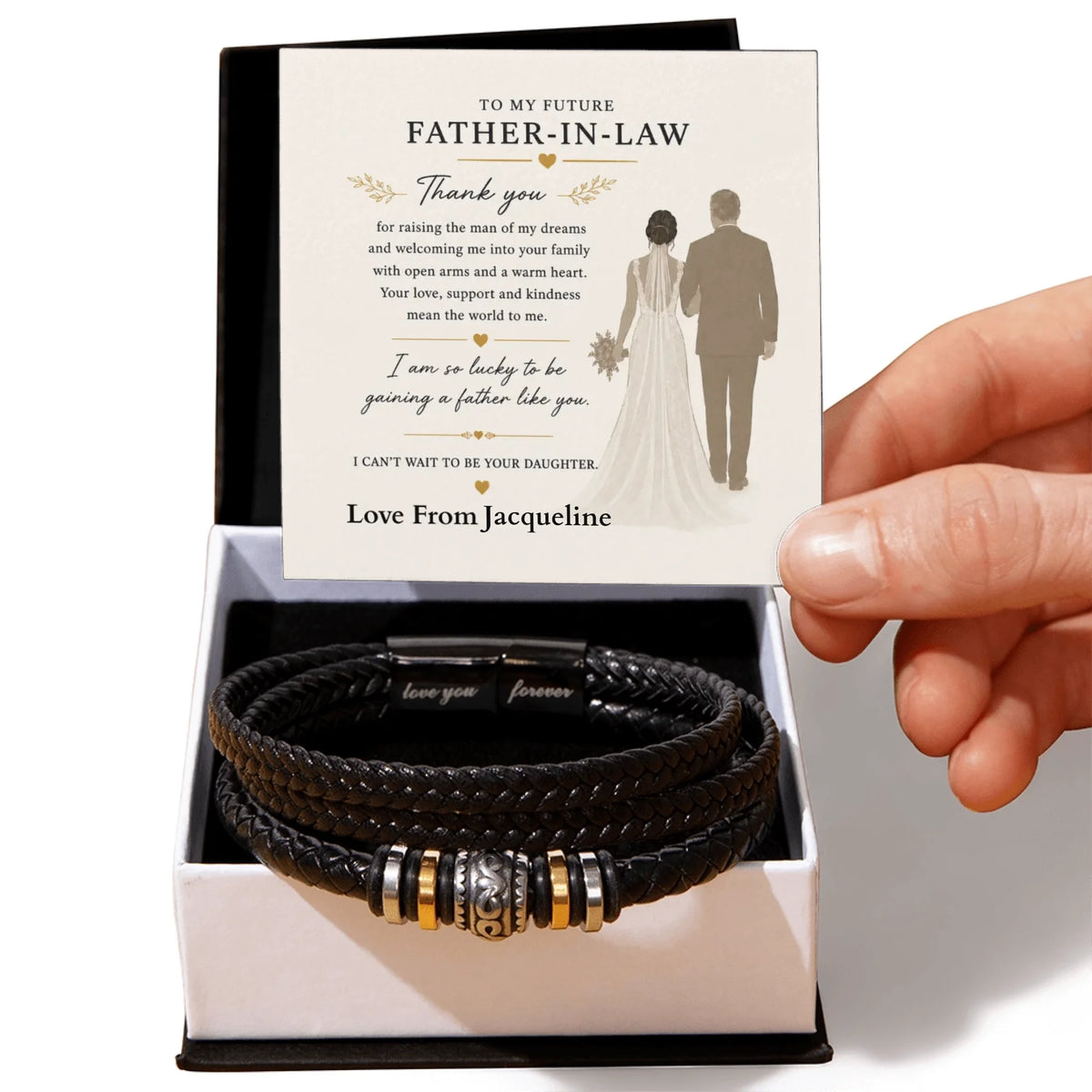 A black braided leather bracelet with gold-toned beads and a silver-toned engraved clasp, presented in an open gift box next to a printed message card addressed to a father-in-law, held by a hand.