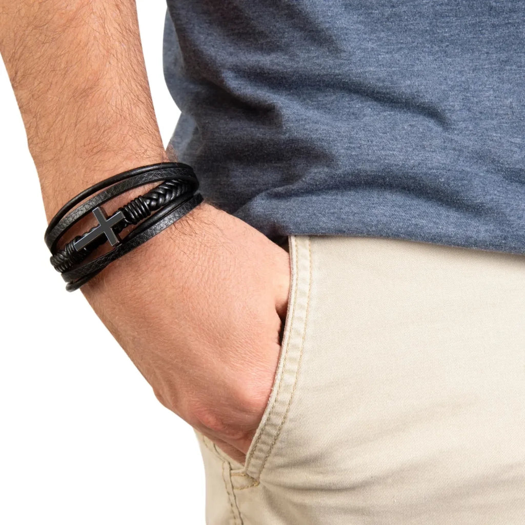 Close-up of a person's wrist wearing multiple black leather bracelets on a neutral background